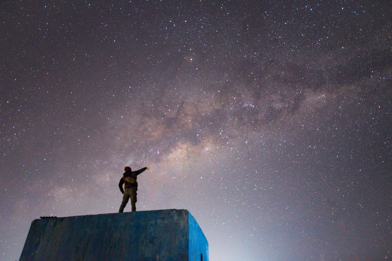 Silhouette of a traveler pointing up at the Milky Way on a clear night